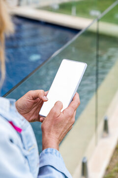 Woman using mobile phone by the pool, empty white screen mockup. Close up.