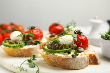 Tasty bruschettas with capers, vegetables and mozzarella served on white marble board, closeup