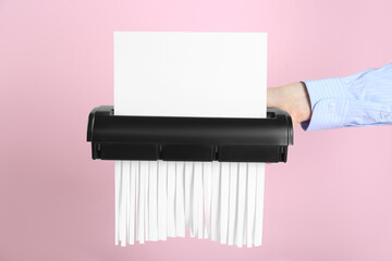 Woman destroying sheet of paper with shredder on pink background, closeup - obrazy, fototapety, plakaty