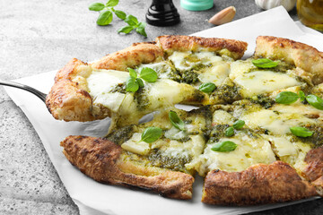 Taking slice of delicious pizza with pesto, cheese and basil on grey table, closeup