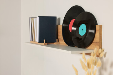 Wooden shelf with vinyl records and books on white wall