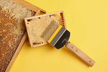 Hive frames with honeycombs and uncapping fork on yellow background, flat lay. Beekeeping