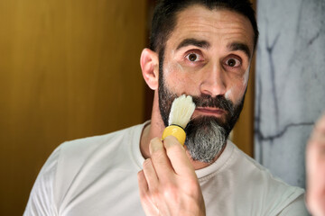Young man soaping his face with a brush to shave his beard