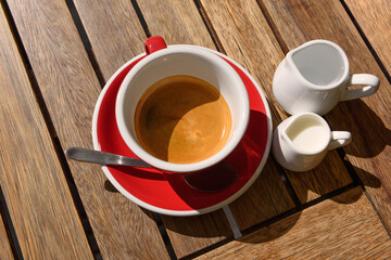 Cup of aromatic hot coffee, milk and water on wooden table, above view