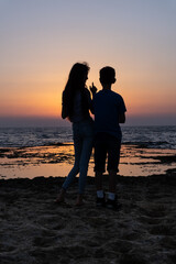 Teenagers, young woman and man speaking and looking at the sunset over the sea in israel. Friendship in childhood silhouette