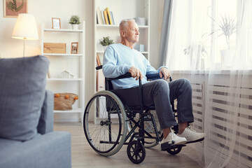 Content pensive senior man sitting in wheelchair and looking out window while dreaming to walk again