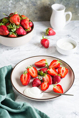 Fresh sliced strawberries and yogurt on a plate on the table. Healthy vitamin dessert. Vertical view