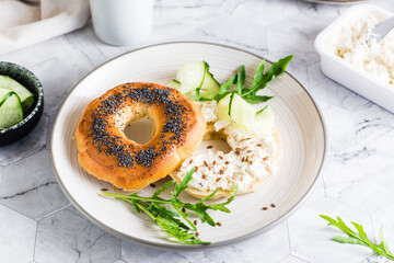 Bagel sandwich with cream cheese, cucumber and arugula on a plate on the table. Homemade breakfast