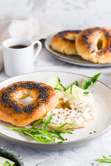 Bagel sandwich with poppy seeds with ricotta, cucumber and arugula on a plate. Vertical view
