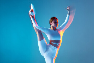 Fototapeta na wymiar Young ballerina training, dancing with raised leg. Slim girl performs modern ballet dance. Motion blur, long exposure