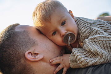 little baby boy on his dad's hands, sucking a pacifier. Spending time outdoors together. Father's...
