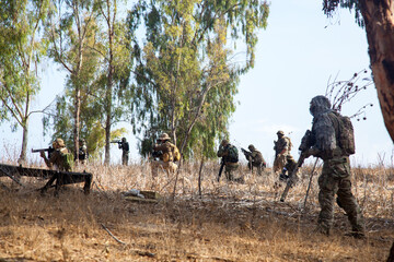 A team of guys in military camouflage is playing airsoft. Team strategy on the field of play. A team of airsoft players moves through a forest area