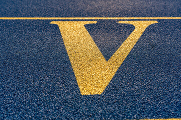 Close up the letter, initial V on a new blue running track with yellow lane lines.