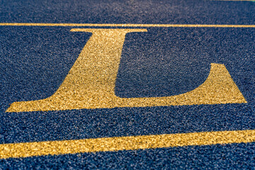Close up the letter, initial L on a new blue running track with yellow lane lines.