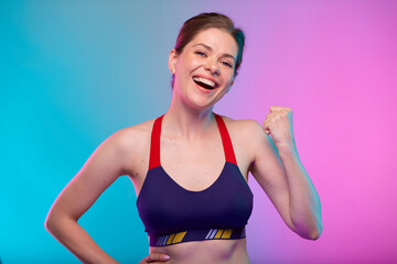 Fototapeta na wymiar Power muscle concept with happy sporty woman in fitness sportswear flexes her arm. Female fitness portrait isolated on neon multicolor background.