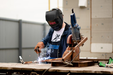 The man works with a welding machine. He is wearing a welder's protective mask and protective gloves. A rare working profession.