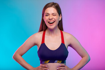 Fototapeta na wymiar Winking sporty woman in fitness bra sportswear. Female coach fitness portrait isolated on neon multicolor background.