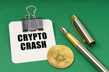 On a green surface, a bitcoin coin, a pen and a sheet of paper with the inscription - Crypto crash