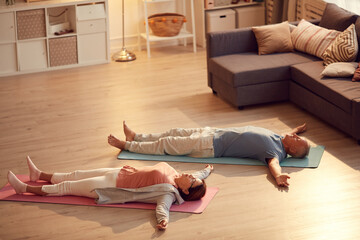 Tired senior couple lying with outstretched arms on floor while relaxing into Shavasana