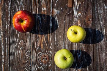 Two ripe green apples and red apple lie on a dark textured wooden table in the kitchen.