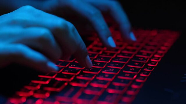 Female fingers are typing on a laptop keyboard with red backlight. Danger or hacker concept. Cybercrime.