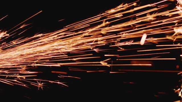 Sparks of angle grinder on black backdrop, closeup. Glowing flow of metal welding spark shining in dark. Industry, tech
