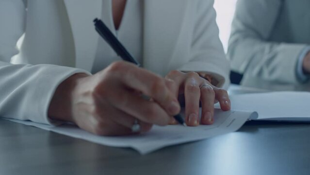 Closeup hand holding pen. Divorcing woman signing documents in attorney office. 
