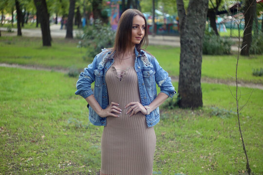 beautiful fashionable blond girl adult  posing in the park in dress and jeens jacket