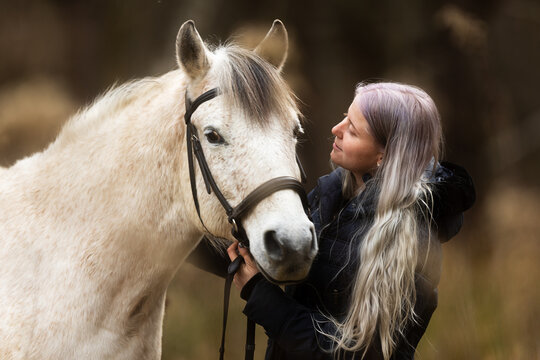 woman with white hair looks closely into the face of her horse