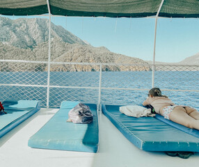 there is a yacht on the seashore. sea with a sandy beach against the backdrop of a mountain. a girl in a bikini is sunbathing on rubber mattresses on board a yacht