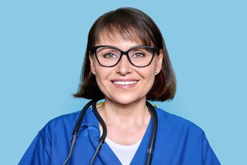 Middle aged female nurse in blue uniform with stethoscope smiling looking at camera - Powered by Adobe