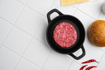 Raw fresh large beef burger on white ceramic squared tile table background, top view flat lay, with...