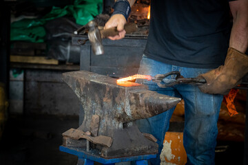Close-up of the hands of a blacksmith using a hammer and anvil to shape a redhot iron blank