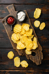 Wavy Potato Chips on old dark  wooden table background, top view flat lay