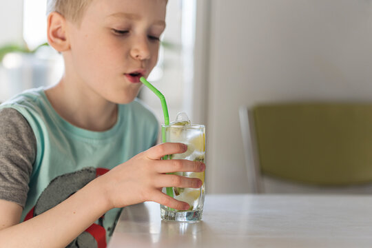 A little boy drinks homemade cold refreshing lemonade with ice cubes, decorated with slices of fresh lime in a steamed glass. the concept of summer
