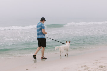 A man and his dog walk the beach on a foggy beach in Pensacola, Florida. 