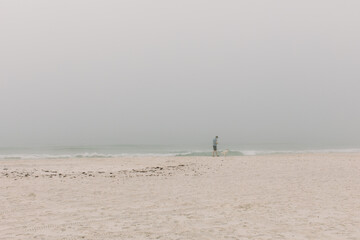 Fototapeta na wymiar A man walks along the beach in Pensacola, FL alone and isolated in the fog and mist. 