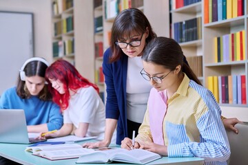 Group of teenage students and teacher study at desk in library