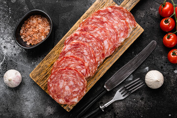 Thinly Sliced Milano salami, on black dark stone table background, top view flat lay