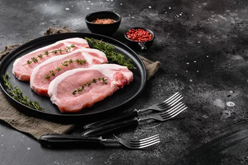 Foto op Canvas Raw pork steak ready for cooking with herbs, on black dark stone table background, with copy space for text © Ilia Nesolenyi