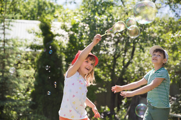 kids blows bubbles in a summer park. children friends have fun summer holidays in nature. happy and...