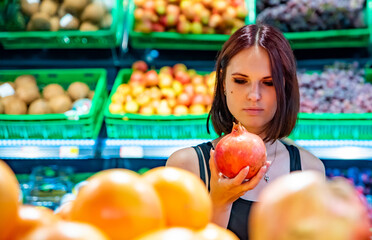 young woman in supermarket choosing pomegranate fruits