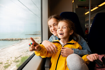 Two sister girls look out the window of a train at the sea.The girls are talking and having fun....