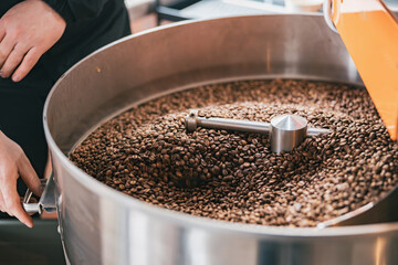 Close up of worker hands roasting coffee beans in roasting machine 