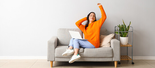 Happy young woman with laptop resting on couch at home