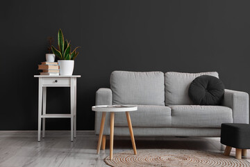 Interior of living room with grey sofa, table and pouf near black wall