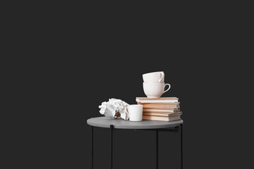 Small table with cups, books and decor near black wall in room