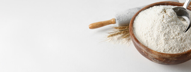 Bowl with wheat flour and rolling pin on white background with space for text