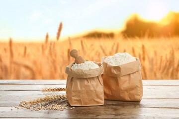 Paper bags with wheat flour on wooden table in field