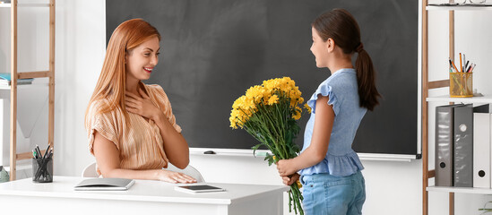 Little schoolgirl greeting her teacher in classroom